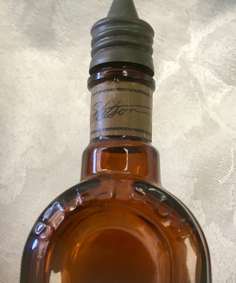 May include: An antique brown glass bottle with a dark metal cap and a paper label. The label has the word "Stetson" written on it. The bottle has a rounded shape and is likely from the early 20th century.