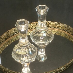 May include: Two clear glass candle holders with a geometric design. The candle holders are sitting on a gold metal tray with a decorative pattern.