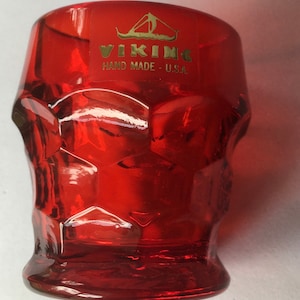 May include: A red glass tumbler with a textured surface. The tumbler has a gold label that reads "VIKING HAND MADE - U.S.A." and a gold image of a Viking ship.
