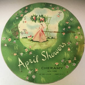 May include: A vintage green and white tin with a floral design and a woman in a pink dress standing in a garden. The text on the tin reads "April Showers" and "Cheramy New York" with a net weight of 6 1/6 oz. and "Comp'd in U.S."