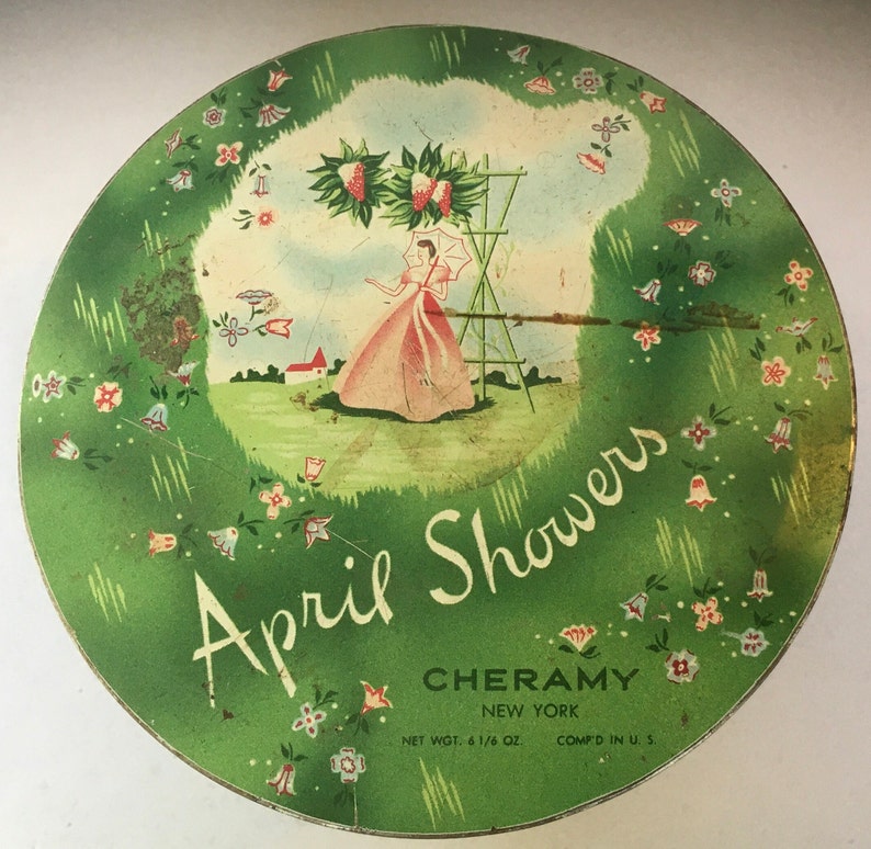 May include: A vintage green and white tin with a floral design and a woman in a pink dress standing in a garden. The text on the tin reads "April Showers" and "Cheramy New York" with a net weight of 6 1/6 oz. and "Comp'd in U.S."