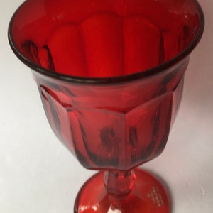May include: A red glass pedestal bowl with a textured design. The bowl has a wide, round base and a deep, round bowl. The bowl is made of clear glass with a red tint.