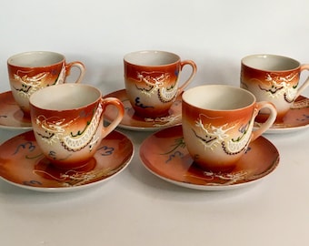 May include: Set of five vintage teacups and saucers. The cups and saucers are orange with a dragon design. The cups have a white interior and a handle. The saucers have a matching design with blue accents.