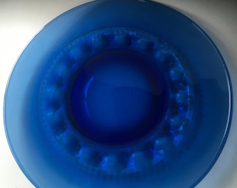 May include: A cobalt blue glass plate with a raised rim and a textured design. The plate is round and has a glossy finish.