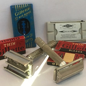 May include: A silver Gillette razor with a red and white box of Thin Gillette blades. There is also a blue box of Gillette Blue Blades and a gray plastic used blade dispenser.