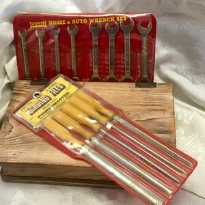 May include: A red case labeled "HOME & AUTO WRENCH SET" contains several wrenches. Below, a package of files with yellow handles is visible. The tools are displayed on a wooden box.