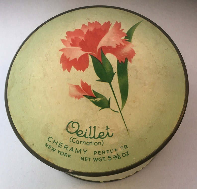 May include: A round, green and white vintage powder compact with a pink carnation flower design. The text on the compact reads "Oeillet (Carnation) CHERAMY PERFUMER NEW YORK NET WGT. 5 3/6 oz."