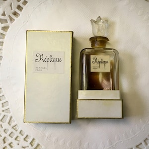 May include: A vintage perfume bottle and box set. The rectangular glass bottle has a clear, tulip-shaped stopper. The box and label read "Réplique, Raphael Paris". The box and base have gold trim.