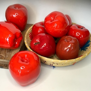 May include: A group of red apples, some in a woven basket and some on a wooden surface. The apples are shiny and appear to be made of ceramic.