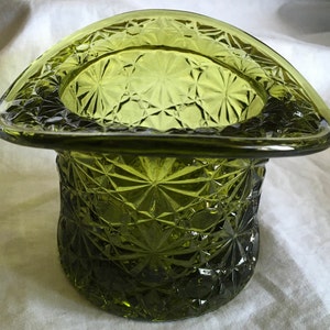 May include: A green glass hat-shaped trinket with a starburst pattern. The hat is made of clear glass with a green tint.