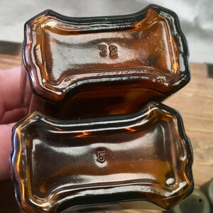 May include: Two amber-colored glass bottles, viewed from the bottom, with a rectangular base and rounded edges. One bottle has the number "32" embossed, the other has "5". The bottles are empty.