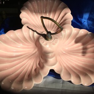 May include: A three-sectioned serving dish shaped like seashells. The dish is made of pink ceramic and has a gold metal handle.