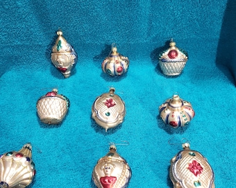 May include: A collection of vintage Christmas ornaments in various shapes, including teardrops and round designs. The ornaments feature gold, red, blue, and green accents. Each ornament has a silver-colored finish and a metal loop for hanging.