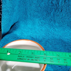 May include: A white ceramic bowl with a brown rim and a floral design. The bowl is being measured with a ruler that reads "NAILS - PENNY SIZE LENGTH IN INCHES".