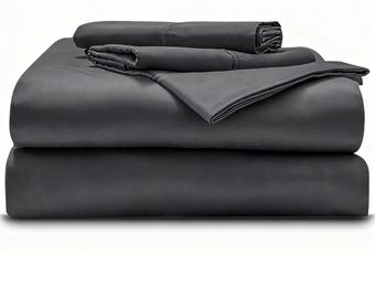 May include: A set of dark charcoal gray bed sheets folded into a neat stack. The collection includes a flat sheet, a fitted sheet, and pillowcases, all featuring a smooth, solid-colored fabric with visible stitched hems along the top edges.