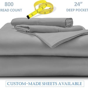 Op de afbeelding: Grijze lakensset met een 800 draadtelling en 61 cm diepe zakken. De lakens zijn gevouwen en gestapeld op een witte achtergrond.  CUSTOM-MADE SHEETS AVAILABLE staat in blauwe tekst onderaan de afbeelding.