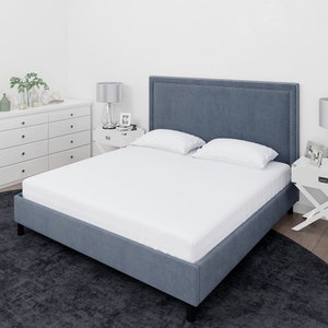 May include: A white fitted sheet on a blue upholstered bed frame with a tufted headboard. The bed is in a bedroom with a white dresser and a lamp on a side table.