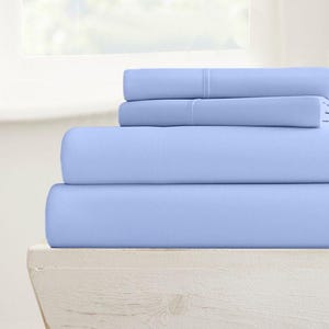 May include: A stack of three light blue fitted sheets. The sheets are folded and stacked on a white wooden surface.