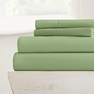 May include: A stack of four sage green fitted sheets. The sheets are folded and displayed on a white wooden surface.