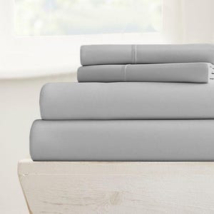 May include: A stack of four gray fitted sheets, folded and displayed on a white wooden shelf.