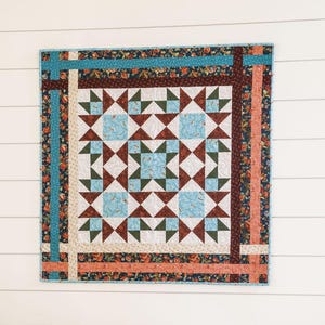 May include: A quilt with a geometric pattern of brown, blue and white triangles. The quilt has a border of floral fabric in shades of orange, brown and blue.