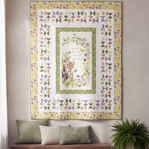 May include: A floral quilt with a white background, featuring a central design with a birdhouse and the text "grow where you are planted." The quilt has a border of butterflies and flowers in shades of green, purple, and yellow.