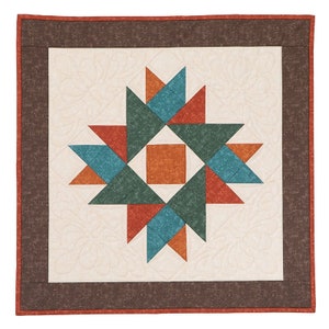 Puede incluir: Una colcha cuadrada con un borde marrón y un diseño central de un patrón de estrella en forma de estallido en tonos de azul verdoso, naranja y verde.