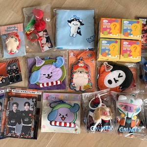 Könnte beinhalten: Eine Sammlung verschiedener Fanartikel, darunter Plüsch-Schlüsselanhänger, Charakter-Taschen, kleine quadratische Schachteln mit der Aufschrift Fandom Art Toy und rechteckige Fotokarten mit zwei Personen, alle einzeln in Klarsichtfolie verpackt.