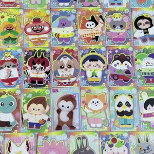 May include: A collection of rectangular trading cards featuring colorful, stylized cartoon characters in various outfits. Each card has a vibrant, patterned background with musical note icons and a holographic finish, displaying diverse animal and human-like figures.
