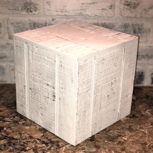 May include: White wooden cube with a distressed finish. The cube has a smooth surface and is perfect for displaying small items.