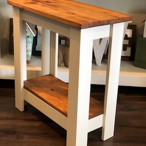 May include: A white end table with a natural wood top and shelf. The table has a simple design with straight legs and a rectangular top.
