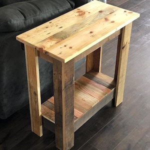May include: A rustic wooden end table with a single shelf. The table is made from reclaimed wood with a natural finish. The table has a simple design with a rectangular top and four legs.