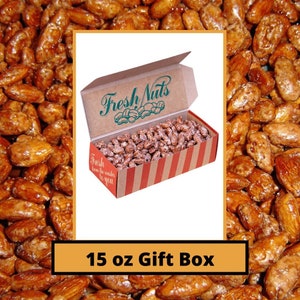 May include: A 15 oz gift box filled with candied almonds. The box is brown with red and white stripes and the words "Fresh Nuts" printed on the top. The almonds are a light brown color and have a shiny glaze.