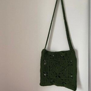 K&ouml;nnte beinhalten: Eine gr&uuml;ne geh&auml;kelte Schultertasche mit quadratischem Design. Die Tasche hat einen langen Riemen und ist aus leichtem Material.