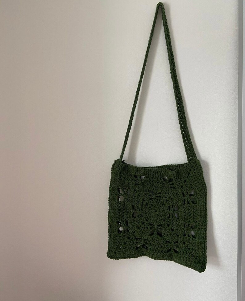 K&ouml;nnte beinhalten: Eine gr&uuml;ne geh&auml;kelte Schultertasche mit quadratischem Design. Die Tasche hat einen langen Riemen und ist aus leichtem Material.