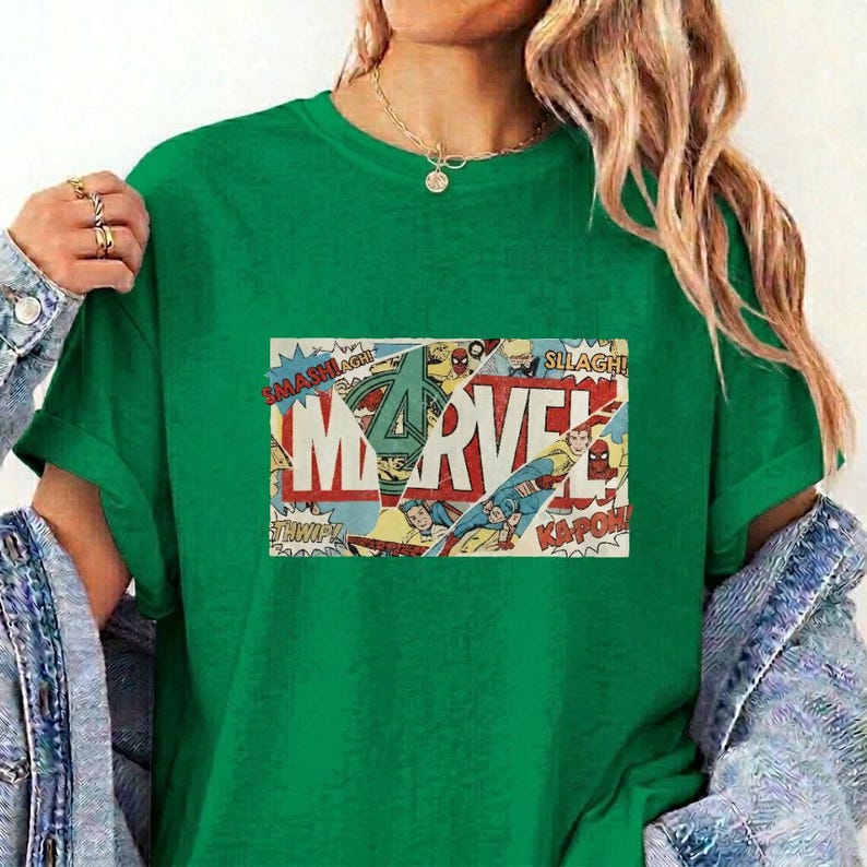 Puede incluir: Una camiseta verde vibrante de manga corta con un estampado gr&aacute;fico rectangular en el pecho. El gr&aacute;fico muestra la palabra MARVEL en letras blancas grandes, superpuesta sobre un collage de c&oacute;mics a color con escenas de acci&oacute;n y efectos.