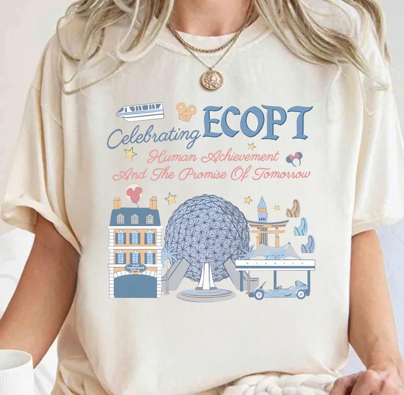 May include: Cream-colored t-shirt featuring a colorful graphic design. The design includes the word "ECOPT" in blue, along with the phrase "Celebrating Human Achievement And The Promise Of Tomorrow." The graphic also depicts various architectural landmarks.