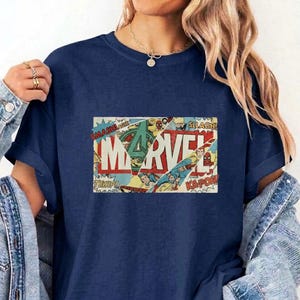 Puede incluir: Una camiseta azul marino con un estampado gr&aacute;fico rectangular de una portada de c&oacute;mic vintage. El dise&ntilde;o muestra la palabra MARVEL en letras rojas grandes, superpuesta con paneles de c&oacute;mic, figuras de acci&oacute;n y onomatopeyas como SMASH.