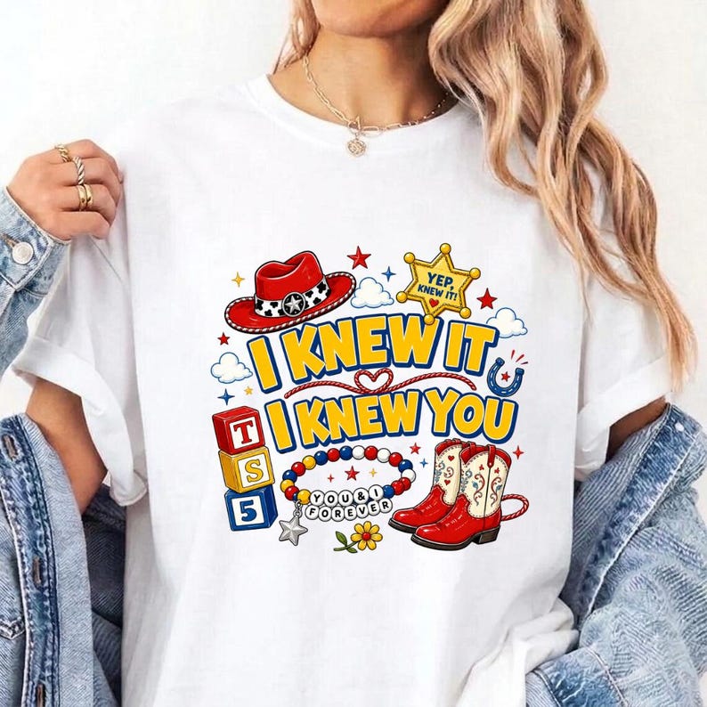 Puede incluir: Una camiseta blanca con un estampado gr&aacute;fico colorido que incluye el texto I KNEW IT I KNEW YOU. El dise&ntilde;o presenta un sombrero de vaquero rojo, una estrella de sheriff amarilla, bloques apilados con T S 5, una pulsera y botas rojas.