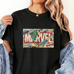 Puede incluir: Una camiseta negra con un estampado gr&aacute;fico rectangular que muestra la palabra MARVEL en letras blancas grandes. El dise&ntilde;o incorpora paneles de c&oacute;mic con varias ilustraciones de superh&eacute;roes, efectos de sonido de acci&oacute;n y un logotipo verde.