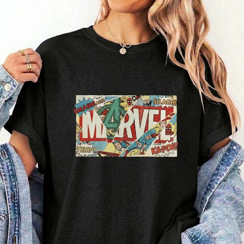 Puede incluir: Una camiseta negra con un estampado gr&aacute;fico rectangular que muestra la palabra MARVEL en letras blancas grandes. El dise&ntilde;o incorpora paneles de c&oacute;mic con varias ilustraciones de superh&eacute;roes, efectos de sonido de acci&oacute;n y un logotipo verde.