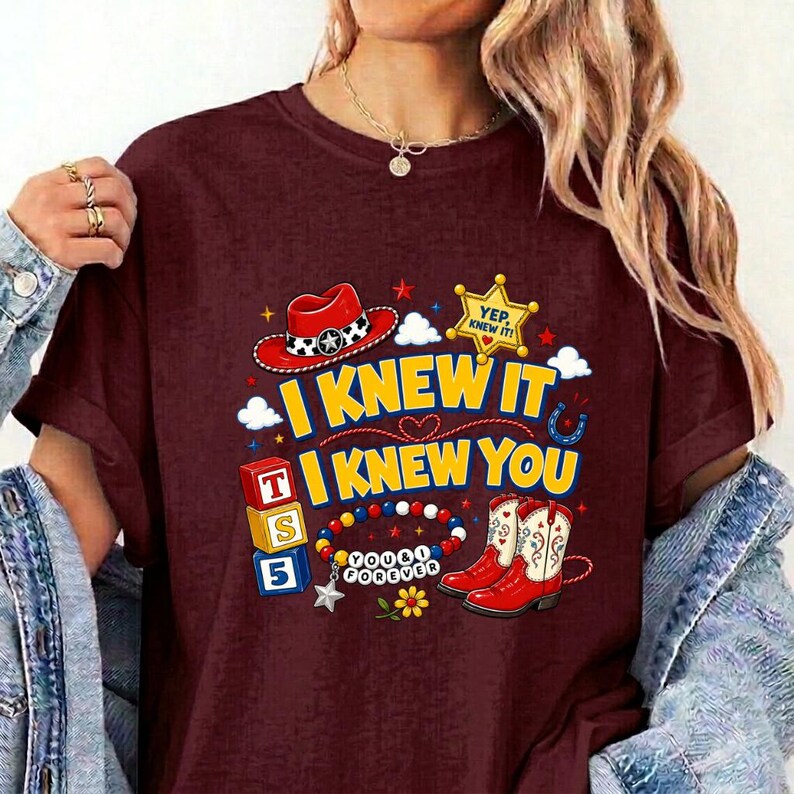 Puede incluir: Una camiseta color granate con un estampado gr&aacute;fico que incluye un sombrero de vaquero rojo, una estrella de sheriff amarilla con el texto YEP, KNEW IT, tres bloques alfab&eacute;ticos coloridos, una pulsera de cuentas con el texto YOU & I FOREVER y botas vaqueras rojas.