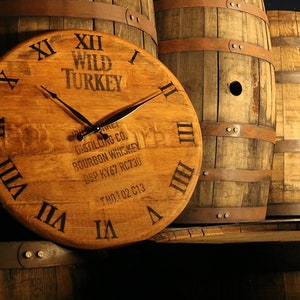 May include: A wooden clock face with Roman numerals and the words "Wild Turkey Distilling Co. Bourbon Whiskey DSP KY67 RC730 TM 01 02 C13"  The clock is made from a repurposed whiskey barrel.