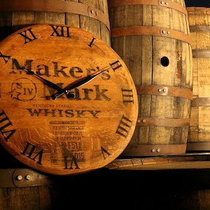 May include: A wooden clock face with Roman numerals and the Maker's Mark Kentucky Straight Bourbon Whiskey logo. The clock is made from a repurposed whiskey barrel.