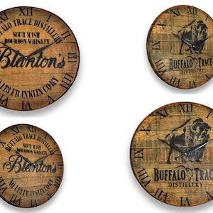 May include: Four wooden barrel head clocks. Two clocks feature the text "Blanton's" and "Buffalo Trace Distillery". The other two clocks feature a bison graphic. All clocks have Roman numeral hour markers and black clock hands.