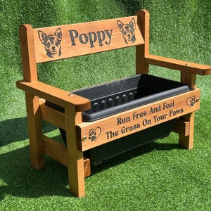May include: A wooden bench planter with a black plastic container. The bench features the name "Poppy" and dog illustrations on the backrest. The text "Run Free And Feel The Grass On Your Paws" is also visible.