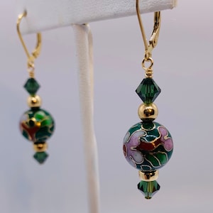 May include: Gold-tone leverback earrings with green, red, and white floral design on a dark green background. The earrings feature gold beads and green crystal accents, creating a classic and elegant look.