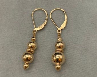 May include: A pair of gold dangle earrings with three round beads on each earring.