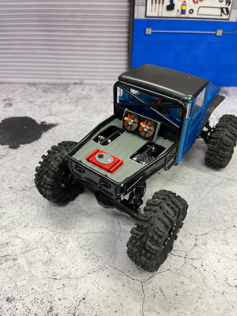 Pode incluir: Caminh&atilde;o de brinquedo preto e vermelho com uma gaiola de seguran&ccedil;a preta e um tanque de combust&iacute;vel vermelho. O caminh&atilde;o tem pneus pretos e uma ca&ccedil;amba cinza. O caminh&atilde;o est&aacute; sentado em uma superf&iacute;cie de concreto cinza.