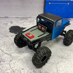 Pode incluir: Um caminh&atilde;o de brinquedo azul e preto com uma gaiola de seguran&ccedil;a preta e um motor vermelho. O caminh&atilde;o tem pneus grandes pretos e est&aacute; sentado em uma superf&iacute;cie de concreto cinza.